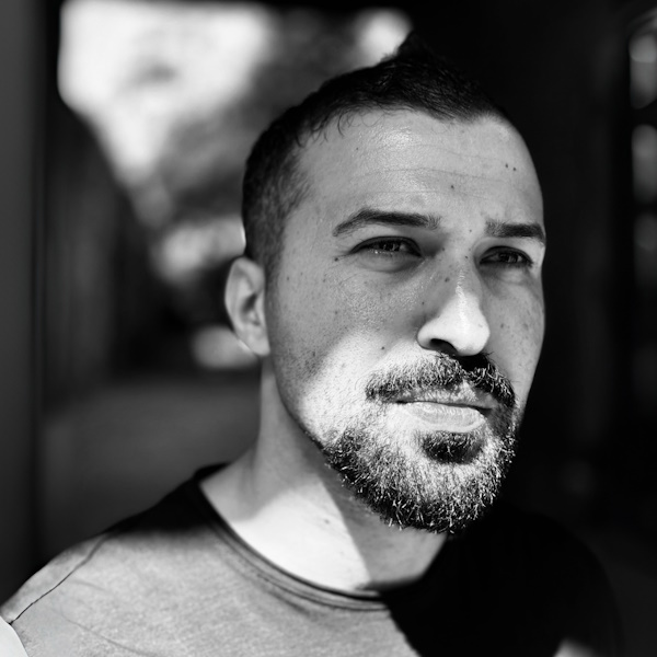 Gazan writer Mohammed Moussa is a handsome mid thirties man in black and white with a shadow cutting across his face he wears a t-shirt and a tidy beard