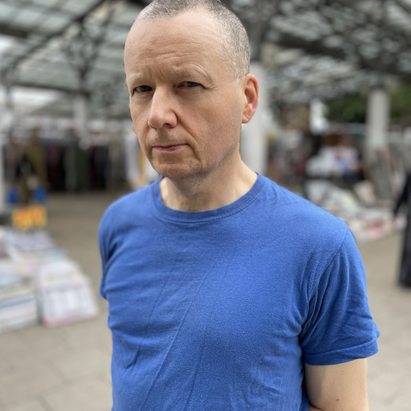 auhtor stewart home standing in a blue t shirt in a london market
